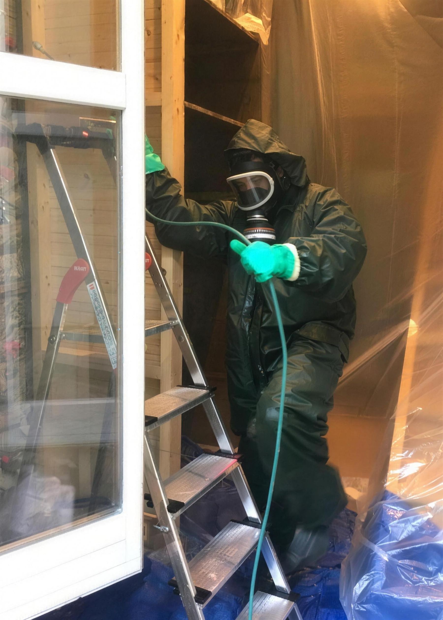 Technicien en combinaison et masque respiratoire qui traite une pièce bâchée contre la mérule